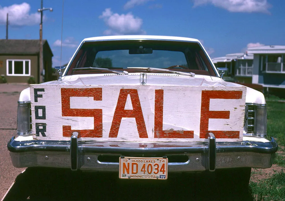 Photo of a large amateur-made 'for sale' sign on the front bumper of a car